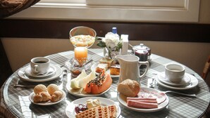 Une table de petit-déjeuner avec divers aliments et boissons, placée devant une fenêtre ornée de rideaux.