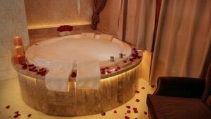 Une baignoire ronde décorée de pétales de roses et de bougies, une chaise et un mur sur lequel est accroché un rideau.