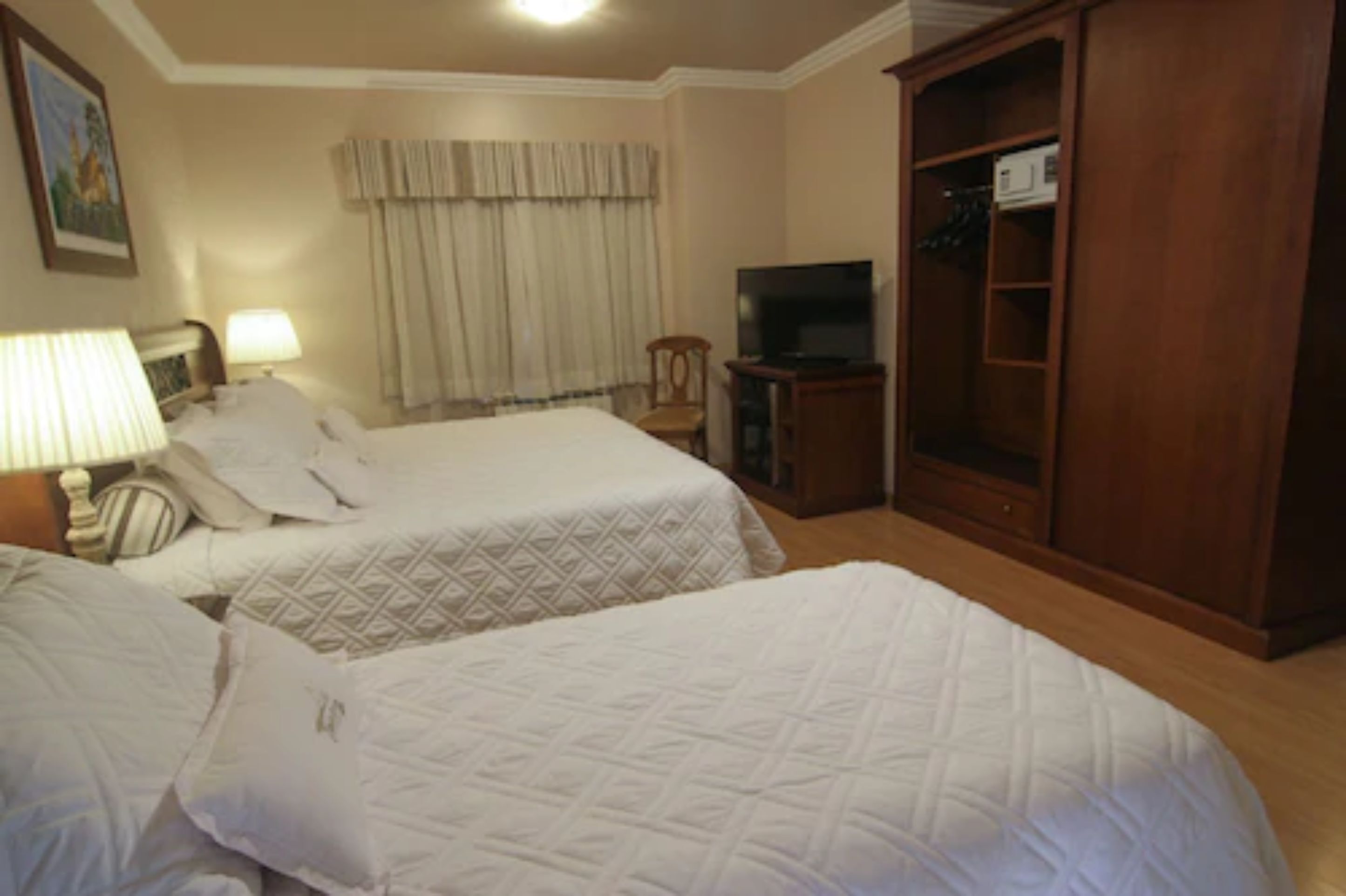 A hotel room with two beds, a television, a wardrobe, and a lamp.