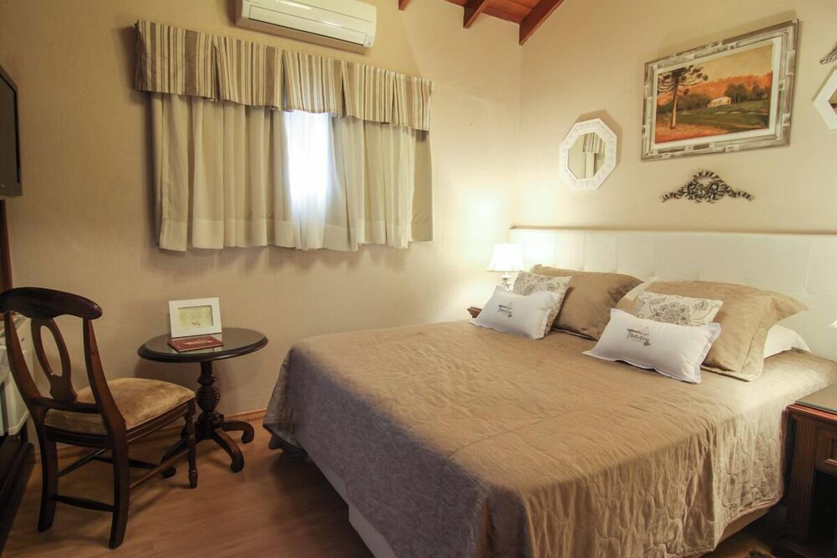 Une chambre à coucher avec un grand lit, une chaise, une petite table et un tableau accroché au mur.