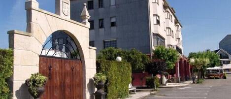 Un edificio con entrada protegida por una reja, cielo despejado y zona de estacionamiento con líneas amarillas.