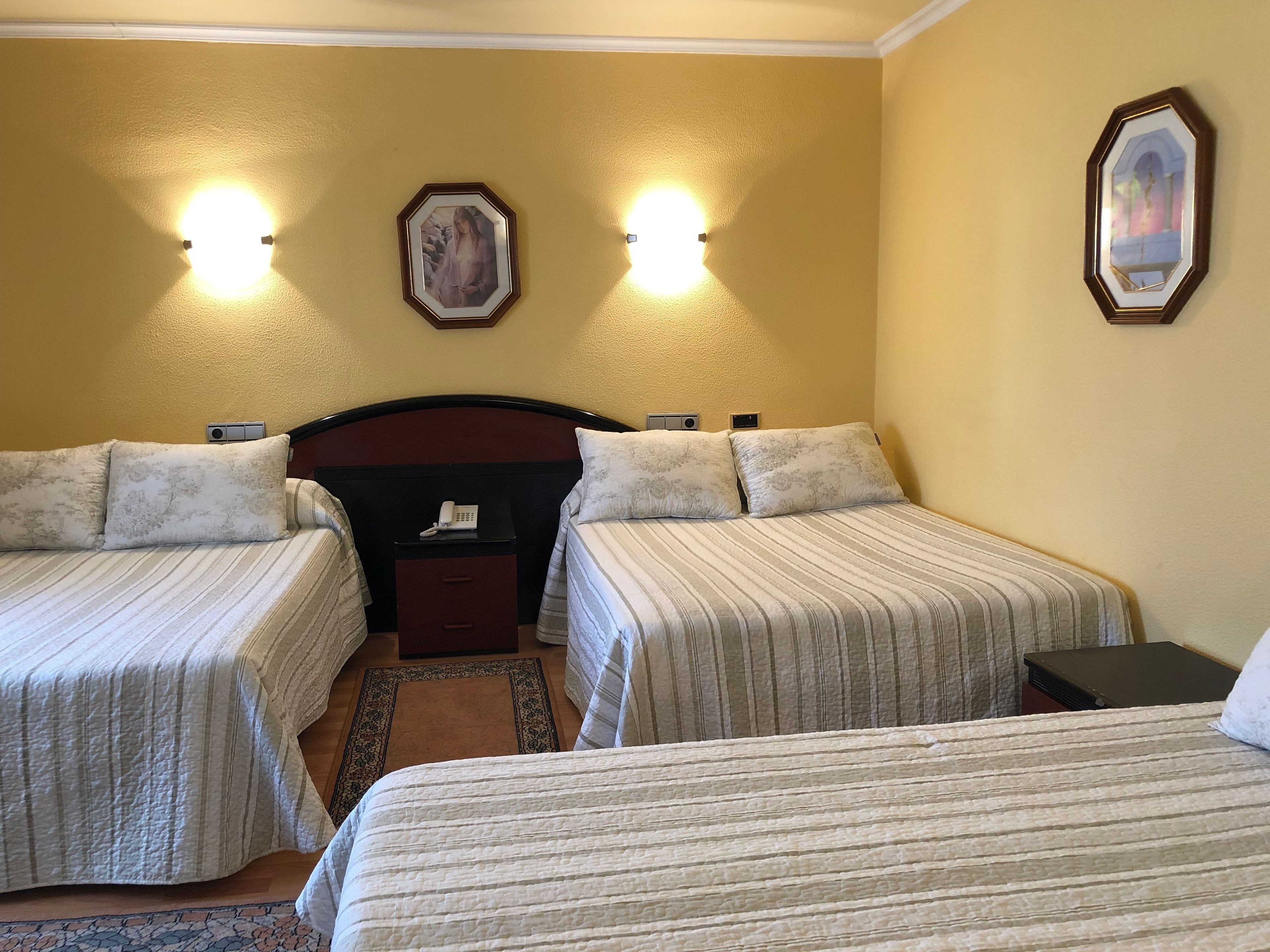 A hotel room with two beds, a nightstand, a telephone, and two wall-mounted lights.