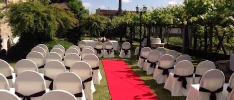 Rows of white chairs with black sashes, a red carpet aisle, and greenery on both sides.