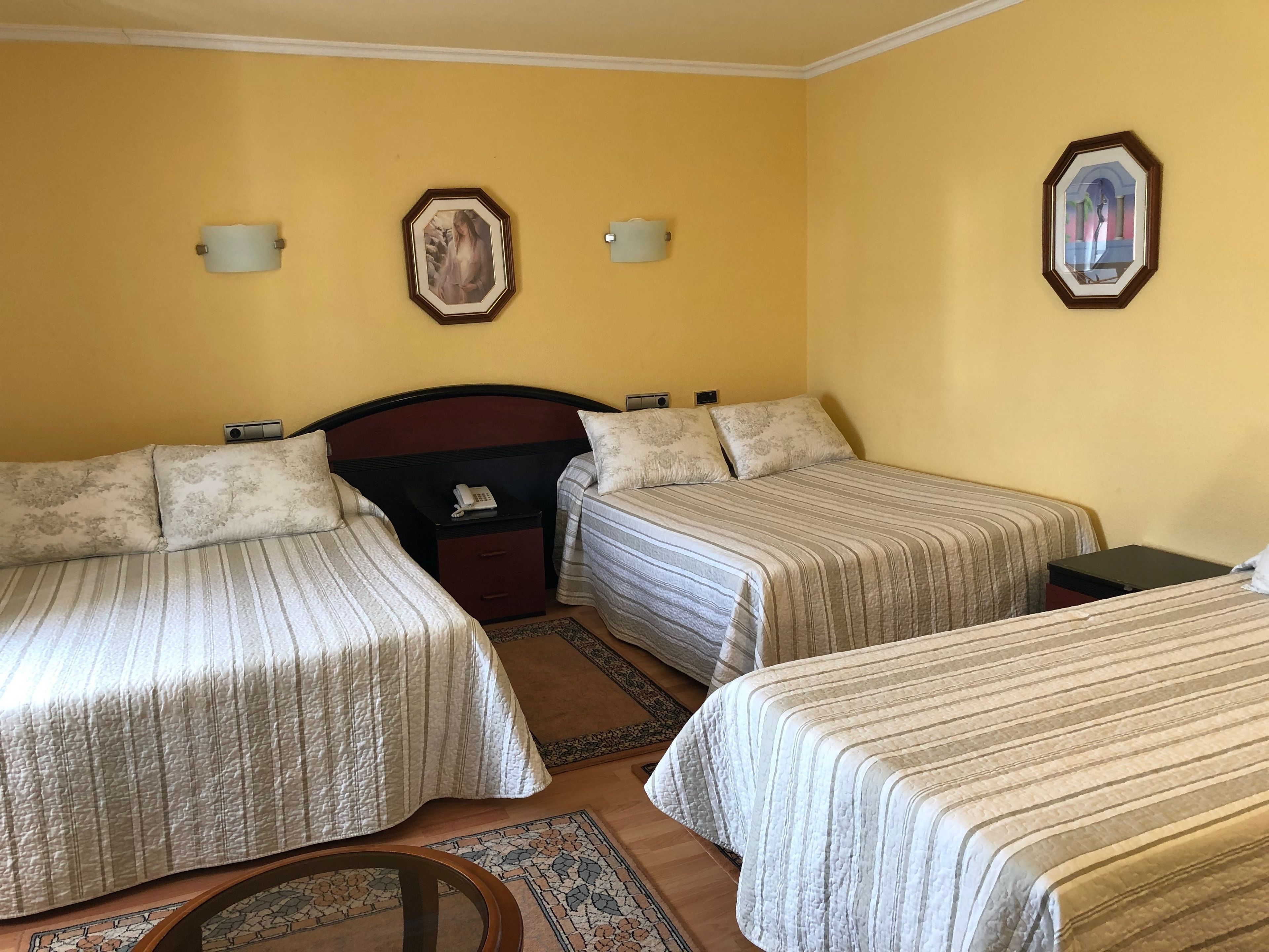 Habitació d'hotel amb dos llits individuals, un capçal de llit de fusta, una taula de nit amb un telèfon i dues làmpades penjades a la paret.