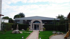 A modern building with a central entrance, a paved pathway leading to it, and a small garden area with rocks and a play structure. - Hotel Sena (Caldas de Reis)