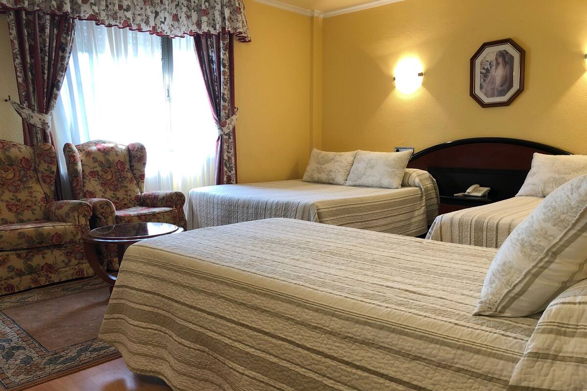 Ein Hotelzimmer mit zwei Betten, einem floralen Sessel, einem kleinen Tisch und einer Wandleuchte.