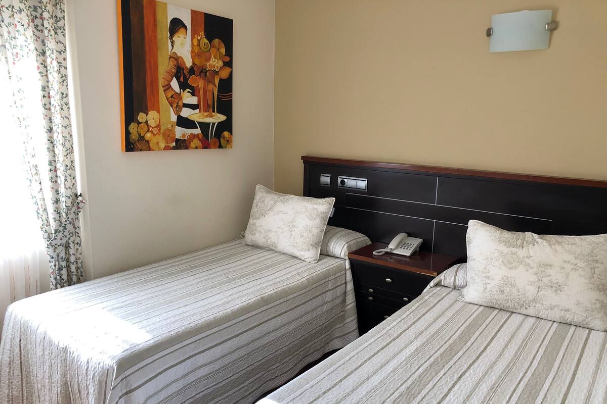 Ein Hotelzimmer mit zwei Betten, einem Nachttisch mit Telefon und einem Gemälde an der Wand.