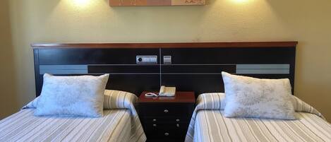 Cama doble con cabecera de madera, dos mesitas de noche y un aplique en la pared.