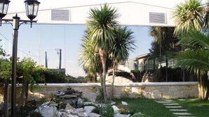 A garden with a rock pond, palm trees, and a stone wall. - Hotel Sena (Caldas de Reis)