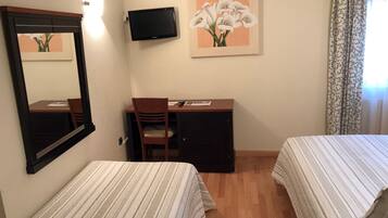 Habitació d'hotel amb dos llits, una taula de treball amb cadira, una televisió de pantalla plana i un quadre de flors a la paret.
