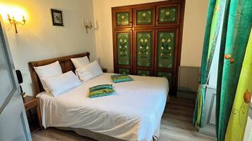 A bedroom with a wooden bed, a nightstand, a wall-mounted lamp, and a green curtain.