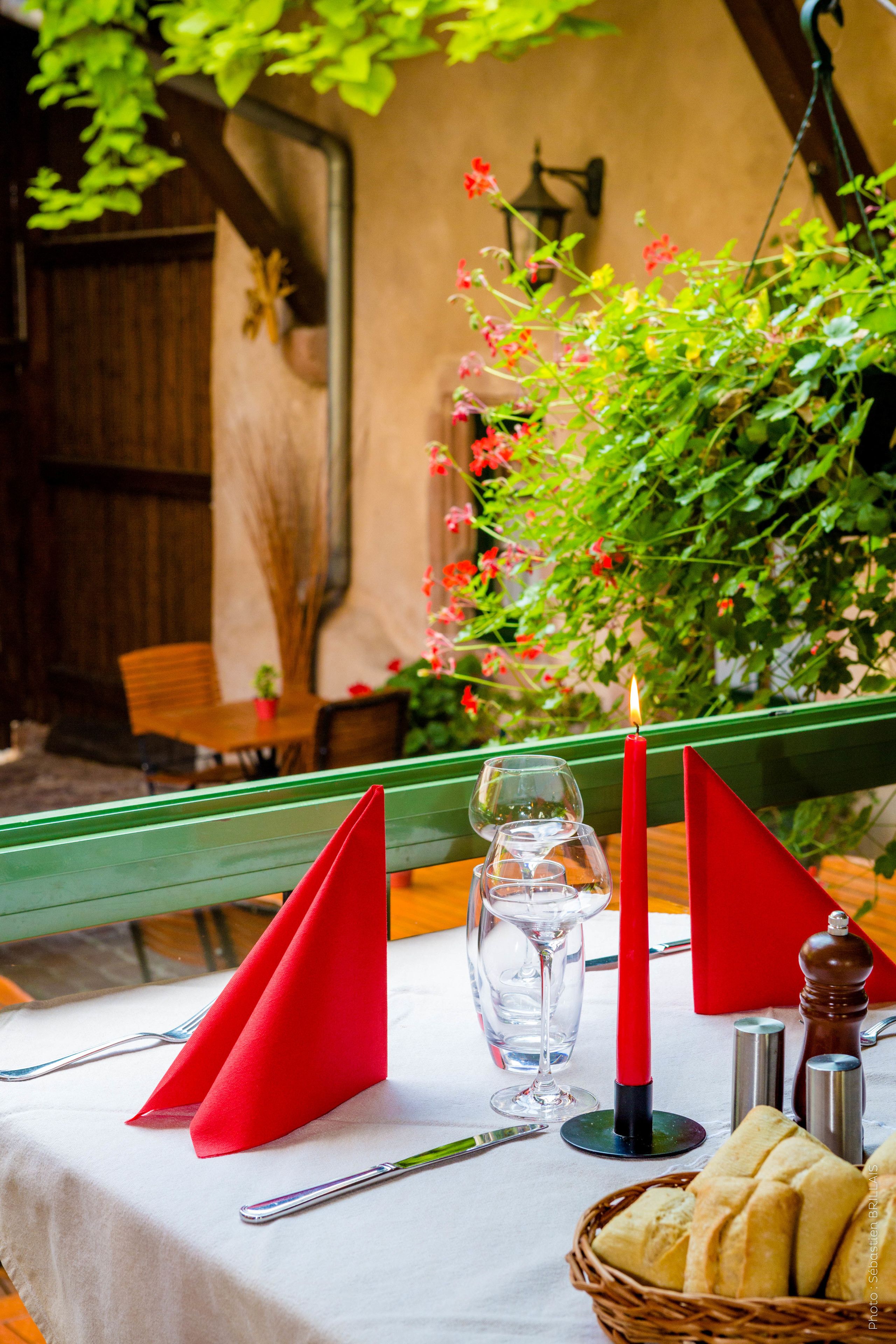 Une table dressée avec des serviettes rouges, un verre d’eau, une bougie, des salières et des poivrières, et un panier de pain.