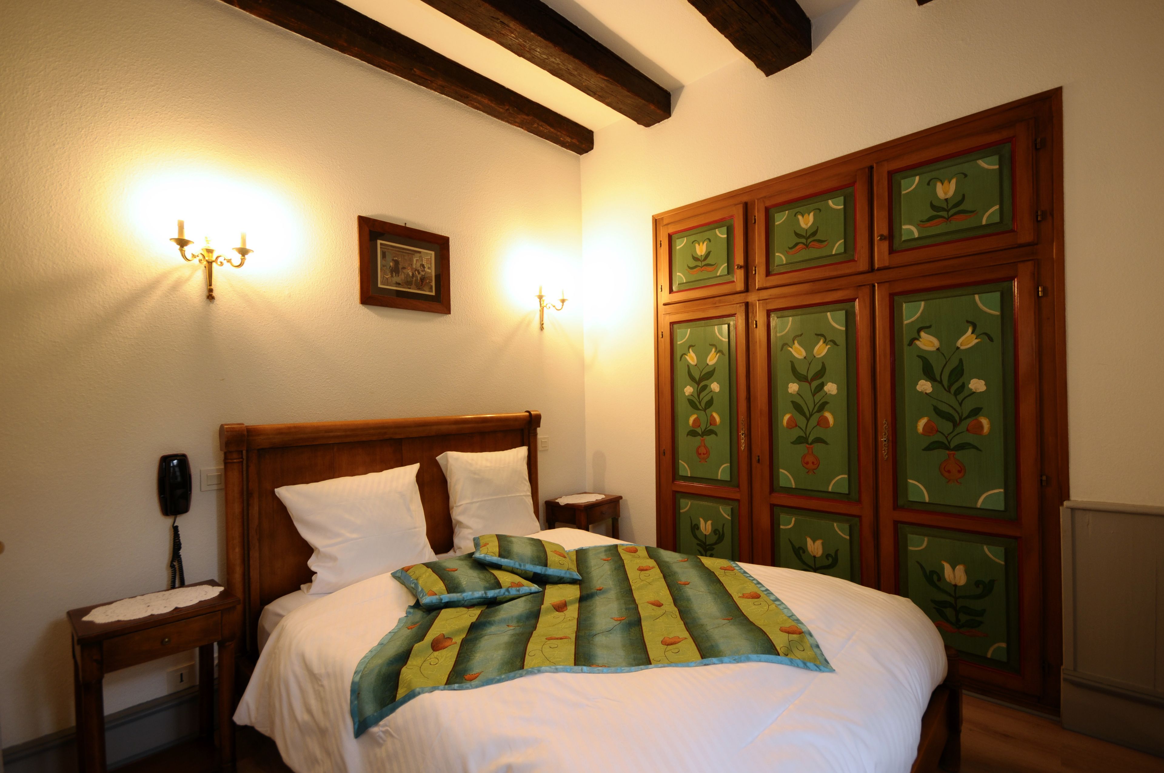 A neatly made bed with a floral bedspread, a wooden headboard, and a nightstand with a lamp.