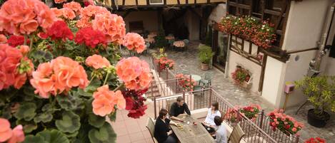 A courtyard with a table and chairs, surrounded by potted plants and flowers.