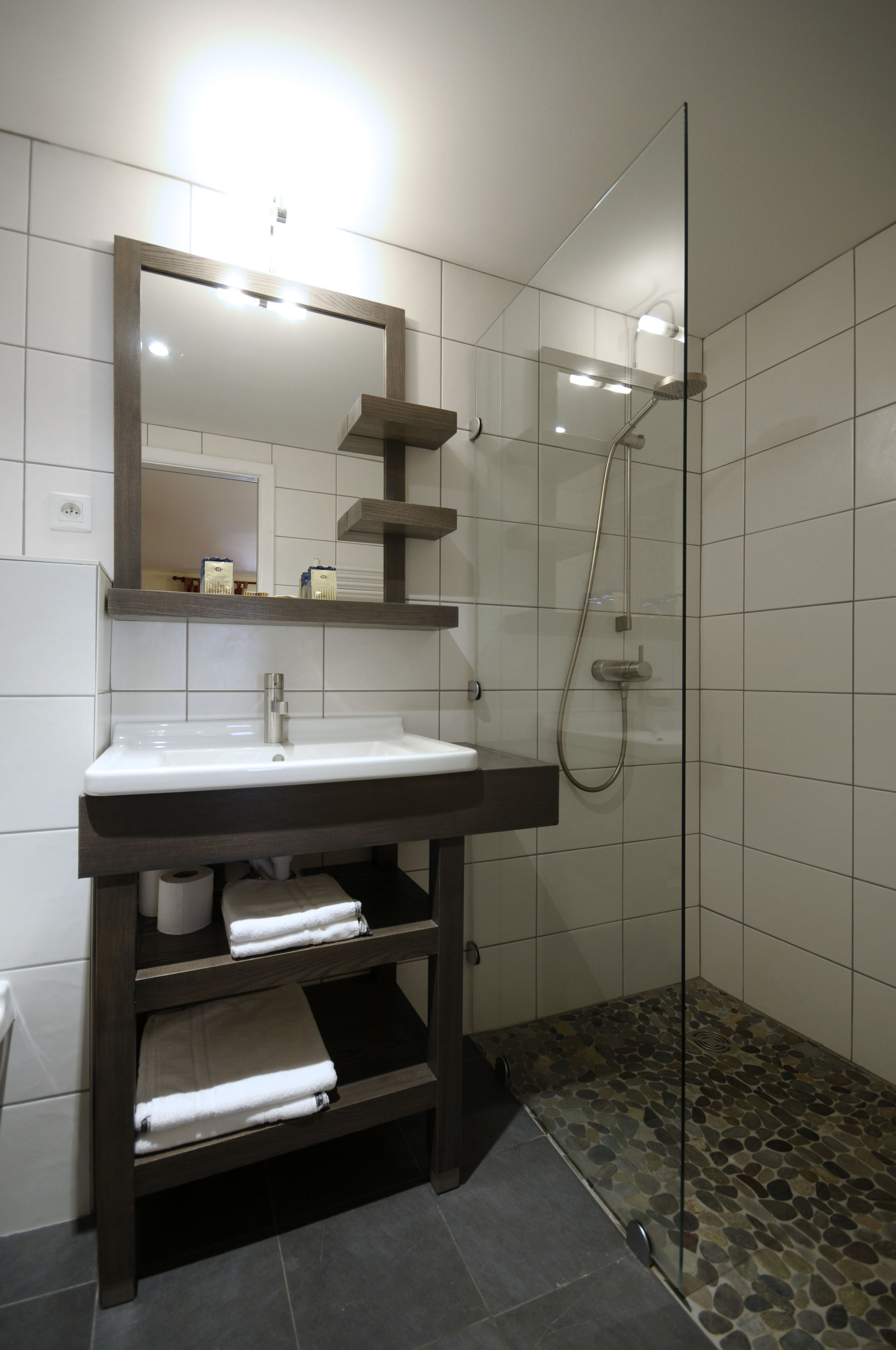 A modern bathroom with a glass-enclosed shower, a white sink with a dark vanity, and a mirror above the sink.