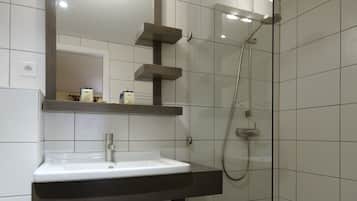 A modern bathroom with a glass-enclosed shower, a white sink with a dark vanity, and a mirror above the sink.