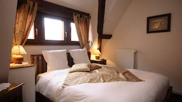 Una cama bien tendida con sábanas blancas y una manta color beige, cabecera de madera, dos lámparas de noche, una ventana con cortinas y un cuadro en la pared.