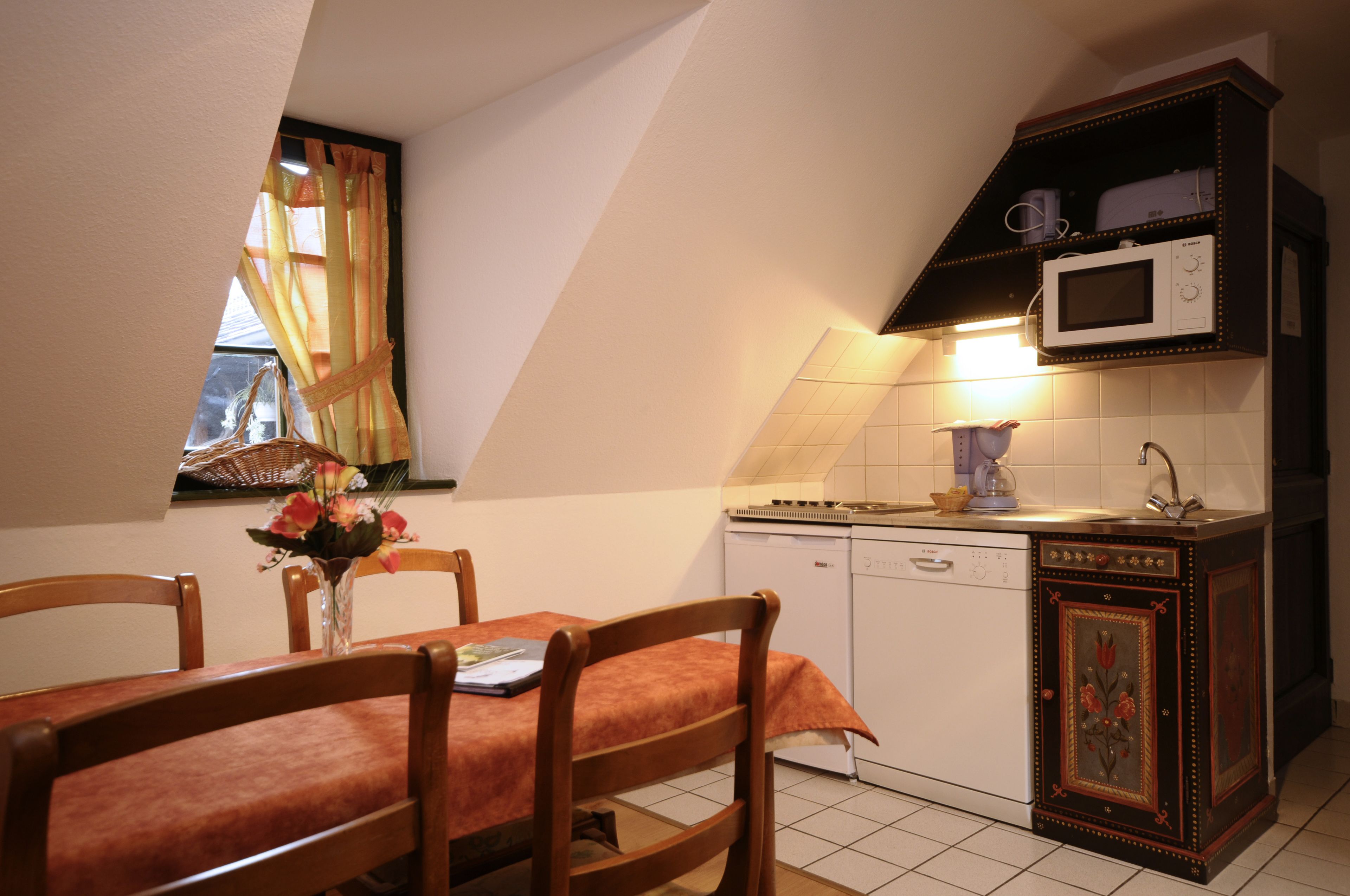 Une cuisine équipée d’un four à micro-ondes, d’une cuisinière et d’un lave-vaisselle. On y trouve une table à manger avec des chaises et un vase rempli de fleurs.