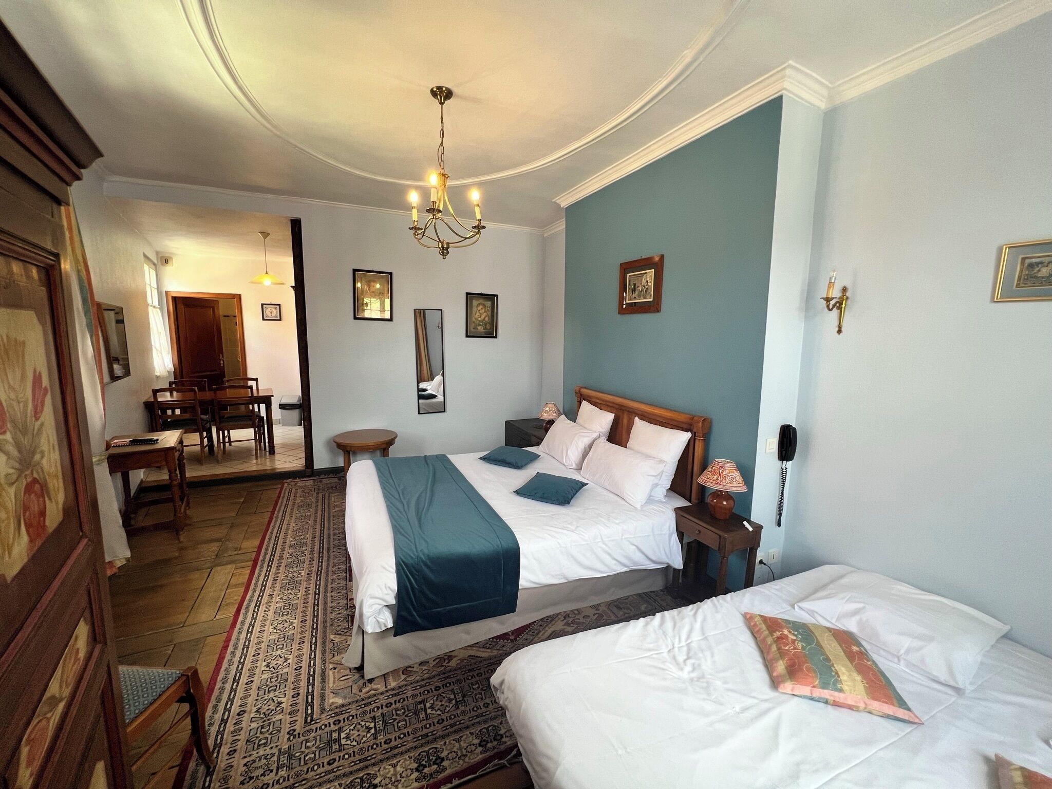 A hotel room with a large bed, a smaller bed, a chandelier, a desk, and a dining area.