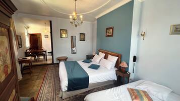 A hotel room with a large bed, a smaller bed, a chandelier, a desk, and a dining area.