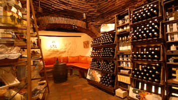 A cozy wine cellar with wooden shelves filled with wine bottles, a wooden barrel, and a cushioned bench.