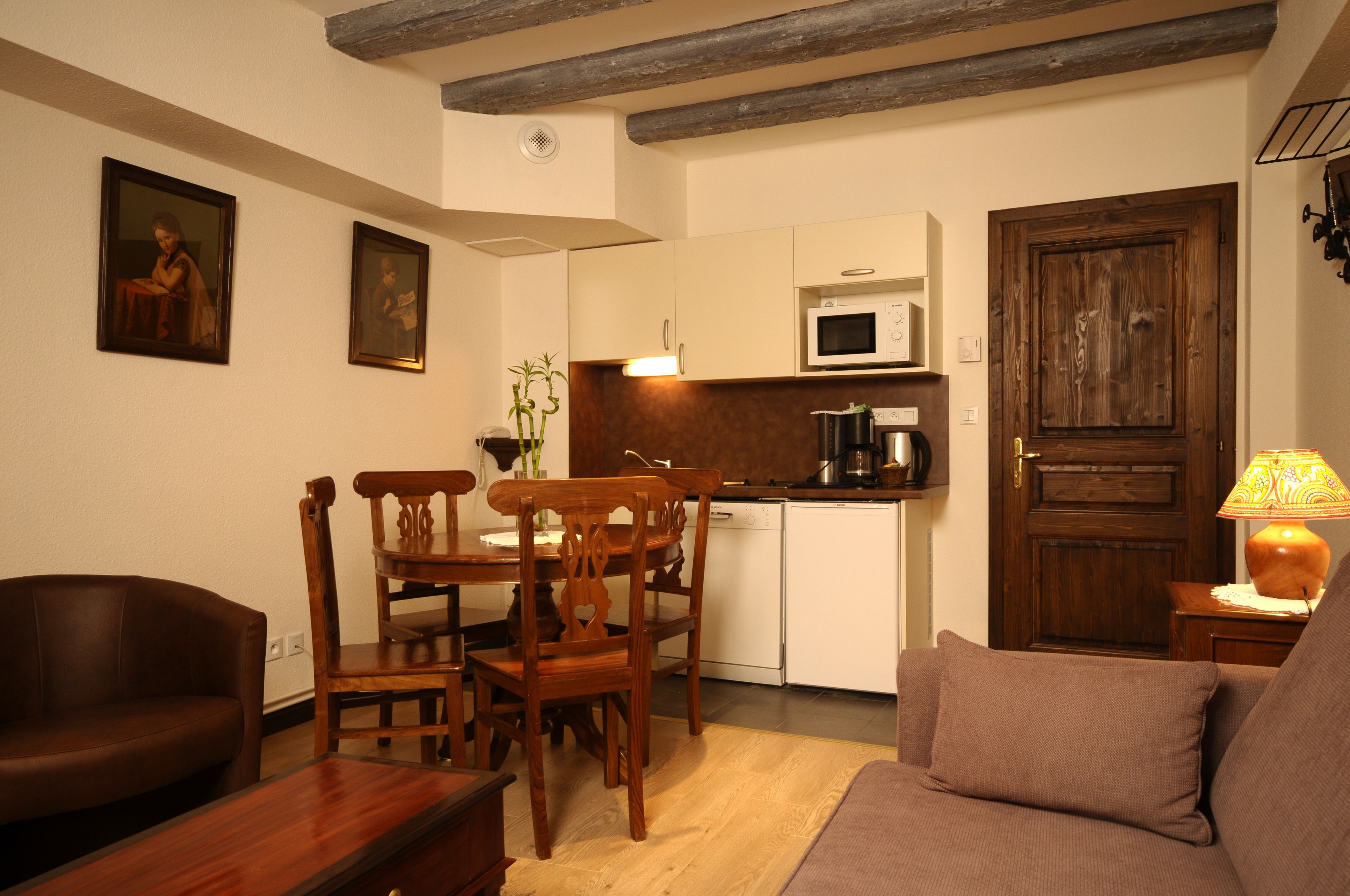 Una sala de estar con una mesa de comedor de madera, sillas, un sofá y una zona de cocina con un microondas y una puerta de madera.