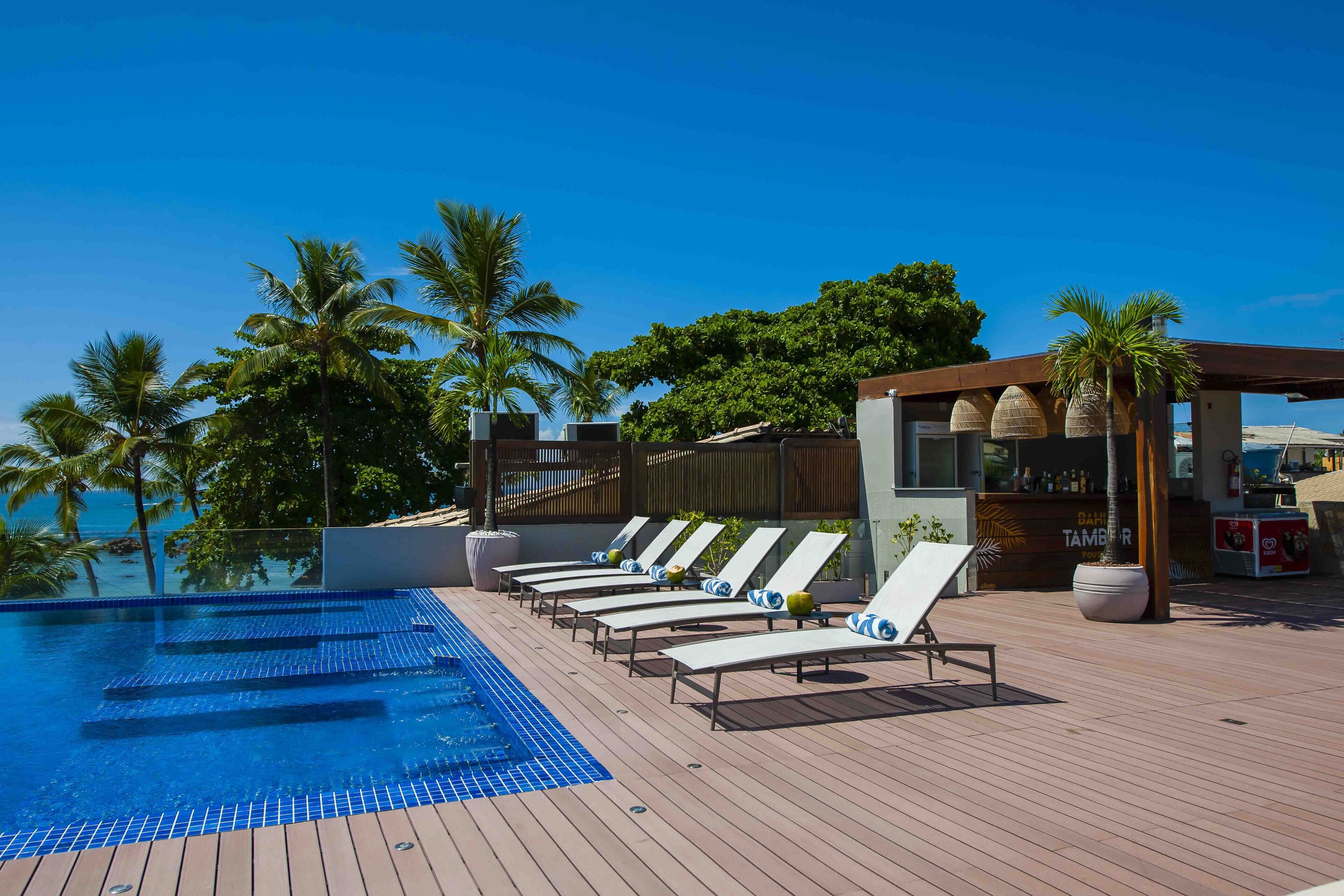 Un espace aménagé au bord de la piscine, avec des chaises longues, une terrasse en bois et une vue sur l’océan.