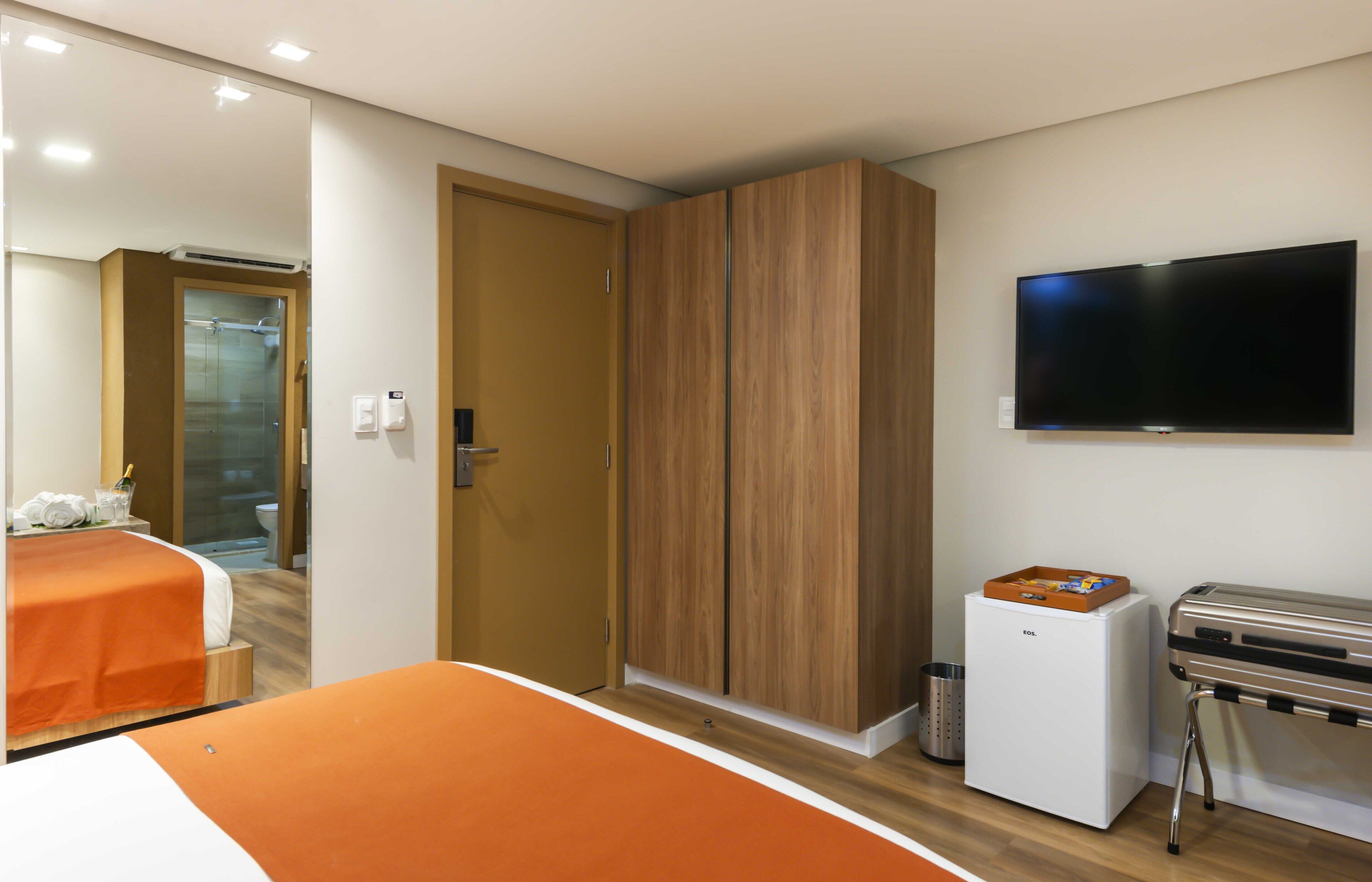 A hotel room with a bed, wardrobe, television, mini-fridge, and a table with a tray.