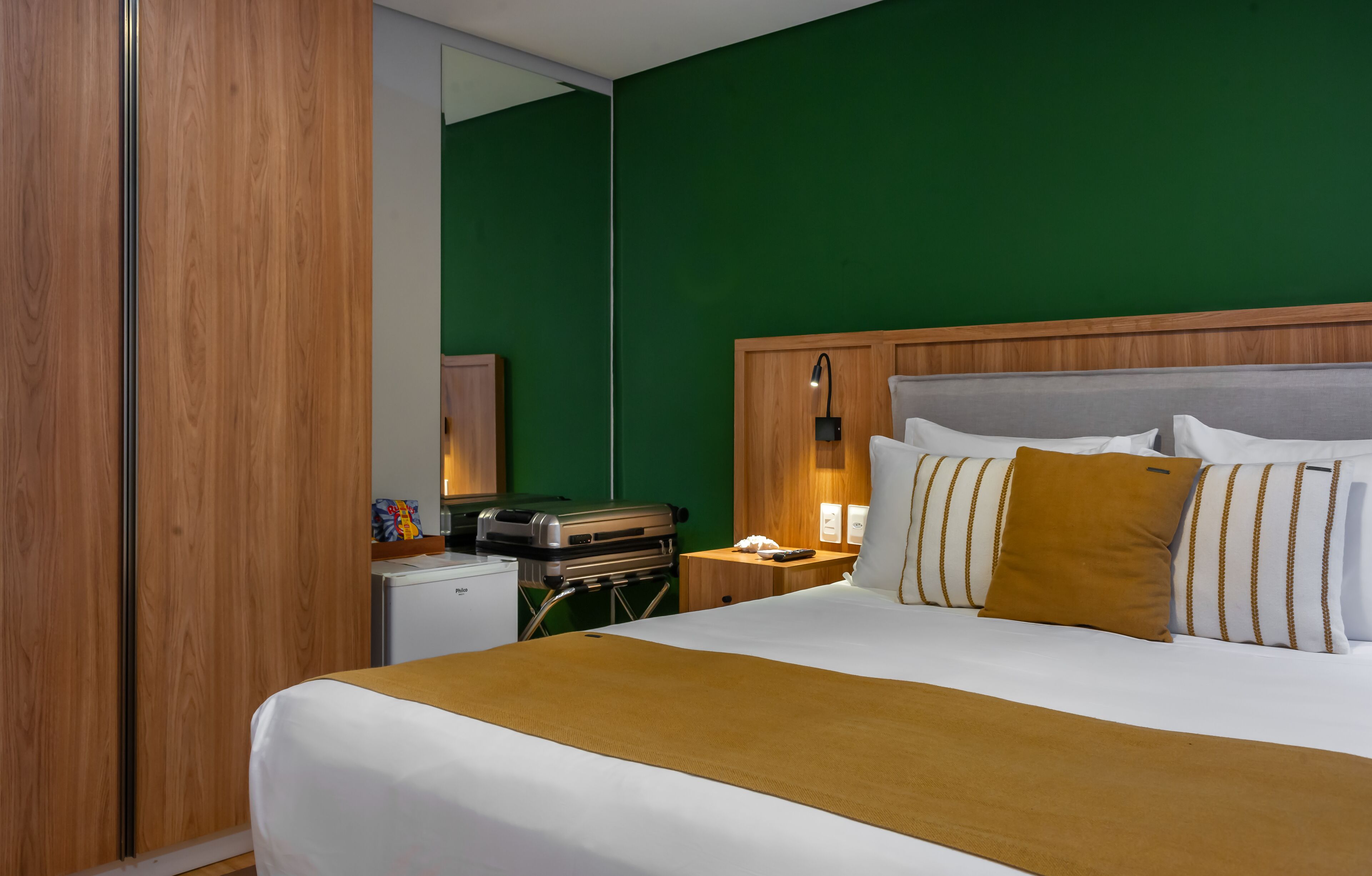 A hotel room with a large bed, a wooden headboard, a green wall, and a small kitchenette with a grill.