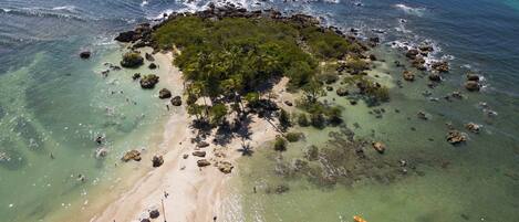 An aerial view of a tropical island with clear waters, sandy beaches, and scattered rocks.