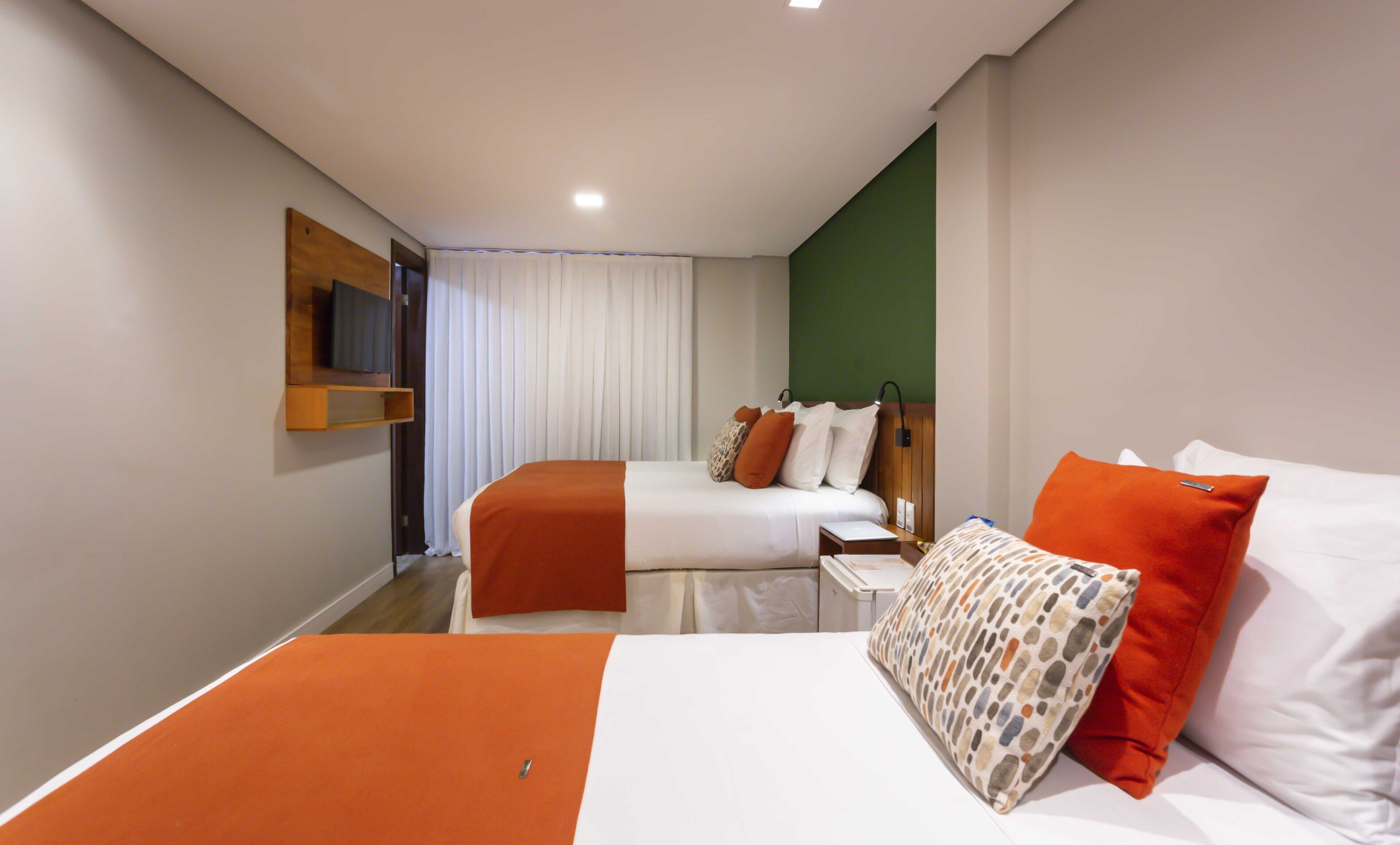Habitación de hotel con dos camas, un televisor en un estante y una pared de acento verde.