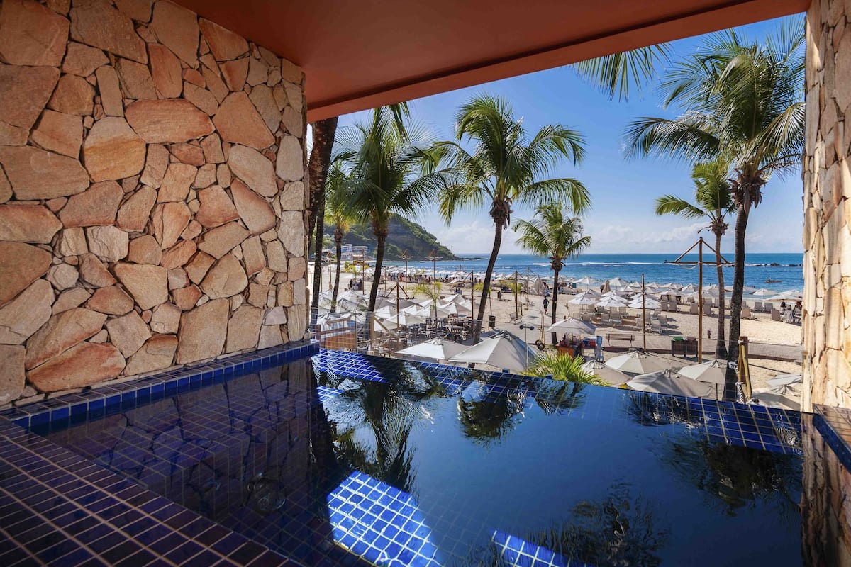Piscina infinita de paredes de piedra con vista despejada a una playa y al océano.