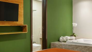 Un baño moderno con una pared verde, un estante de madera, un inodoro blanco, una bañera y una orquídea blanca.