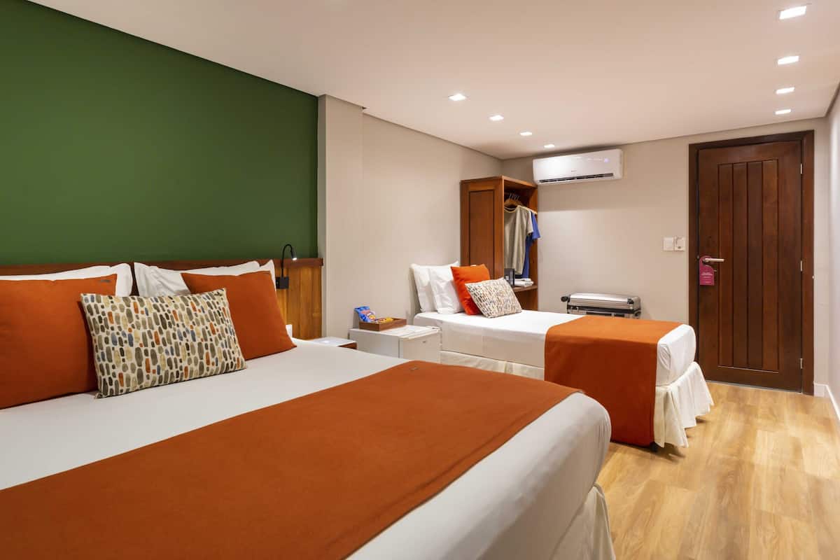 Habitación de hotel con dos camas, un armario, una mesita pequeña y un aire acondicionado.