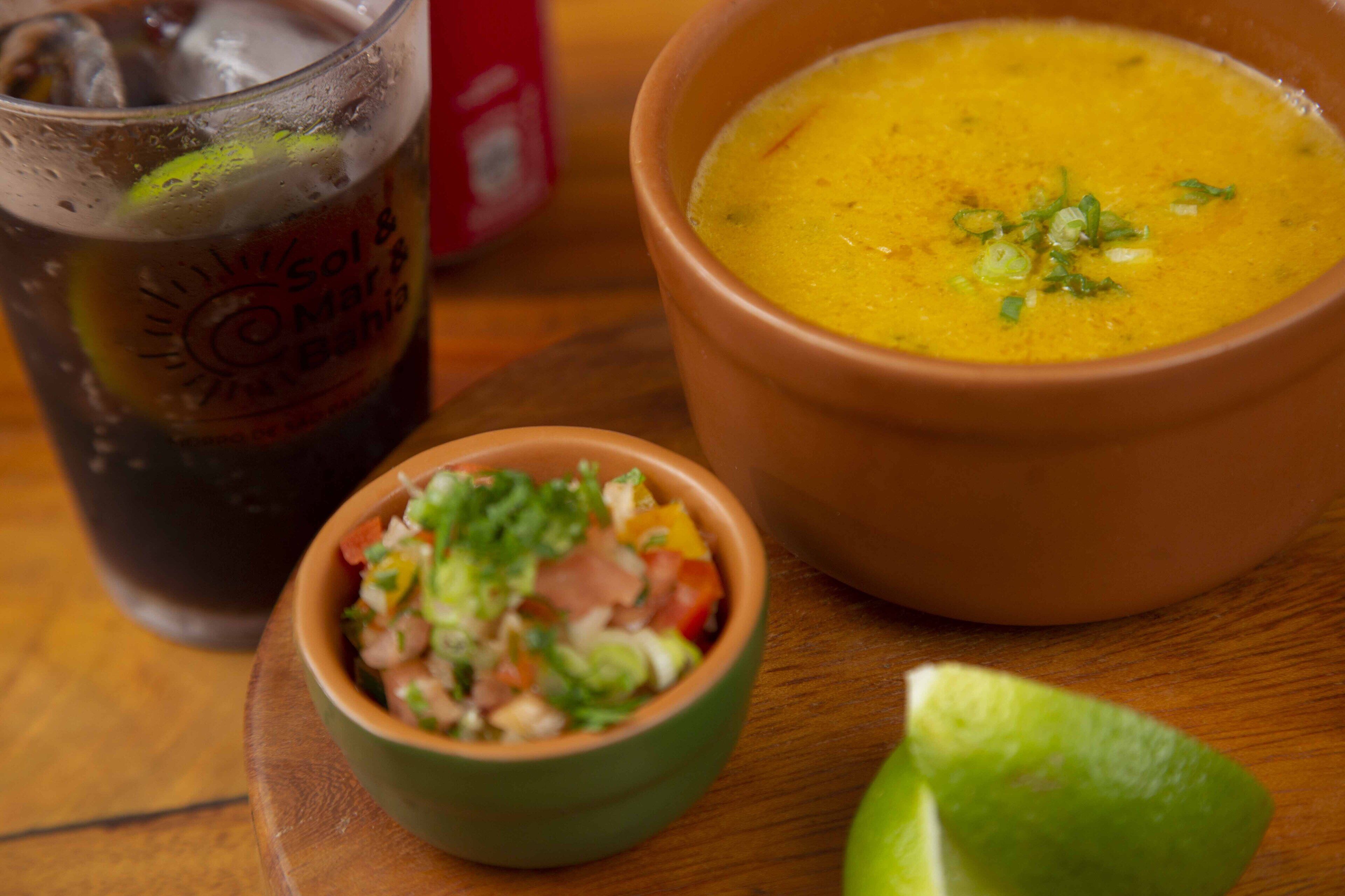 A bowl of soup, a glass of a beverage, and a small bowl of salad on a wooden table.