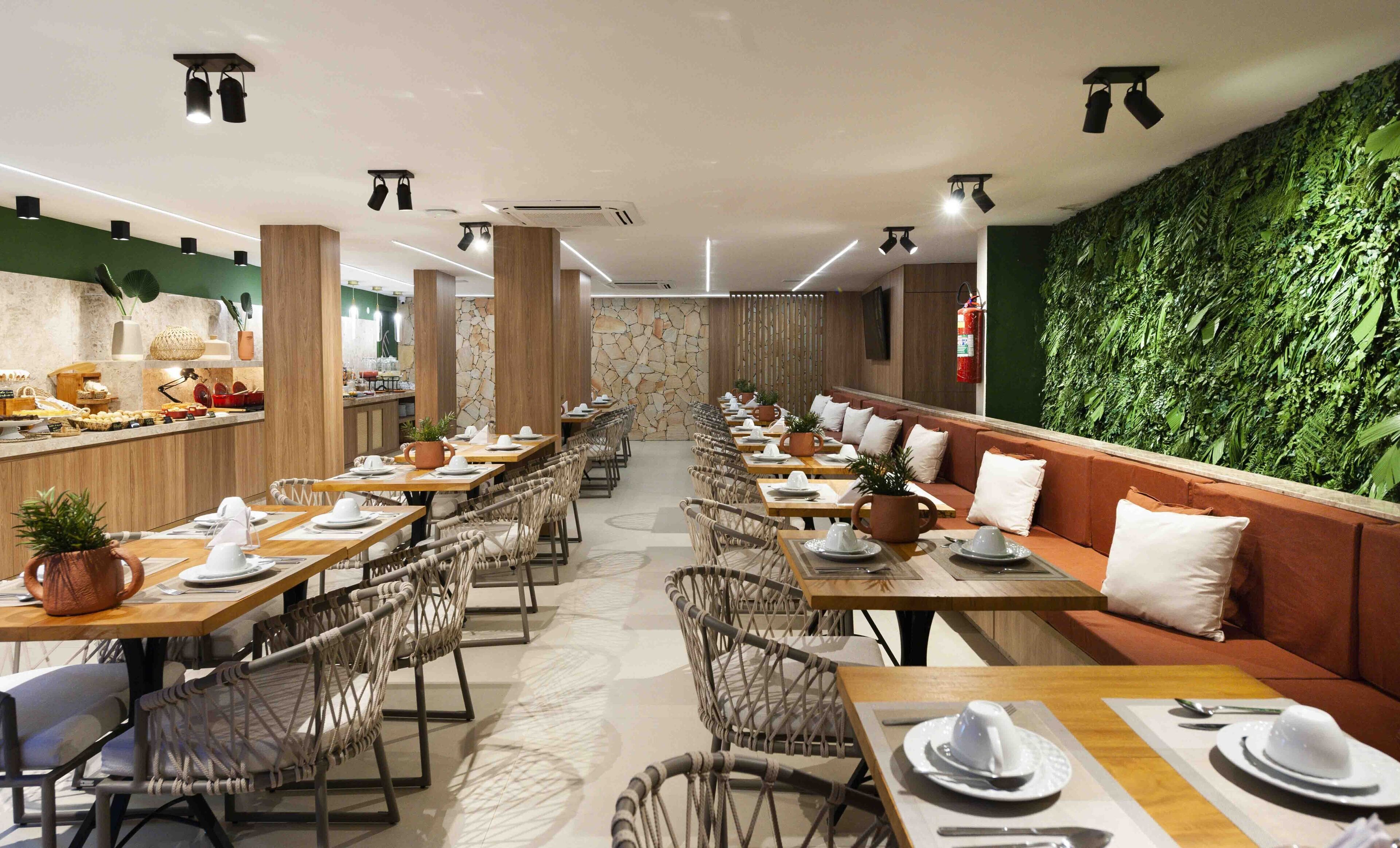 Un ristorante con lunghe tavole comuni, cabine private e una parete verde con vegetazione.