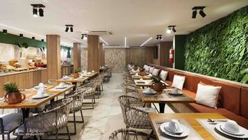 Un ristorante con lunghe tavole comuni, cabine private e una parete verde con vegetazione.