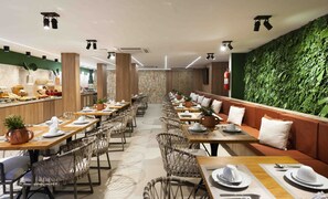 Un restaurante con mesas largas compartidas, cabinas individuales y una pared verde con follaje.