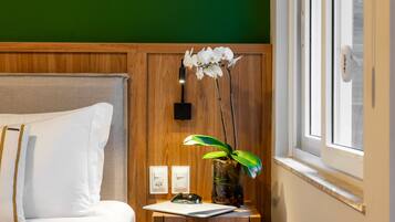 Een keurig opgemaakte hotelkamer met een bed, nachtkastje met een vaas orchideeën, en een raam met uitzicht.
