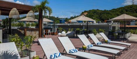 A rooftop lounge area with sun loungers, umbrellas, and potted plants.