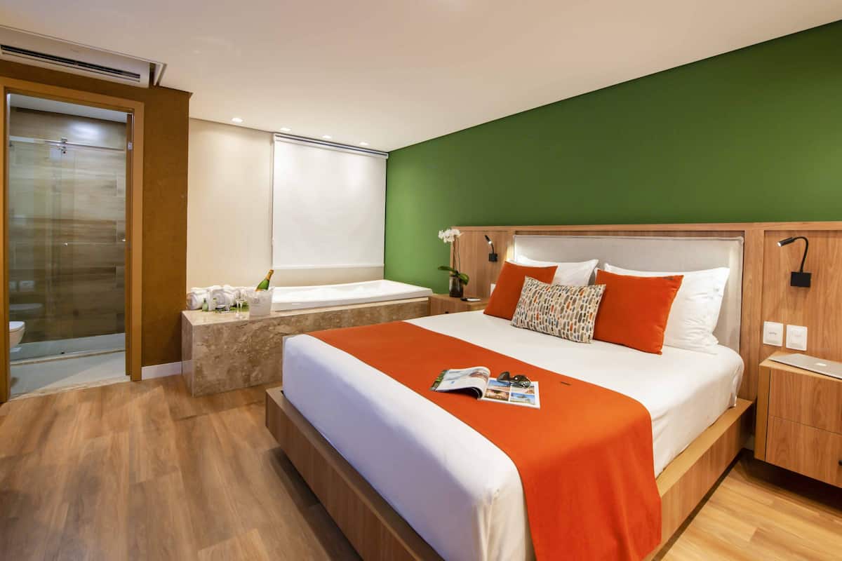Habitación de hotel con una cama grande, una mesita de noche de madera, un cabecero de madera, una pequeña mesa y una pared de acento verde.
