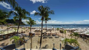A beach with palm trees, umbrellas, and lounge chairs.