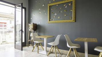A modern interior with a dining area featuring white chairs and a wooden table, a large decorative frame with butterflies, and a view through an open door.