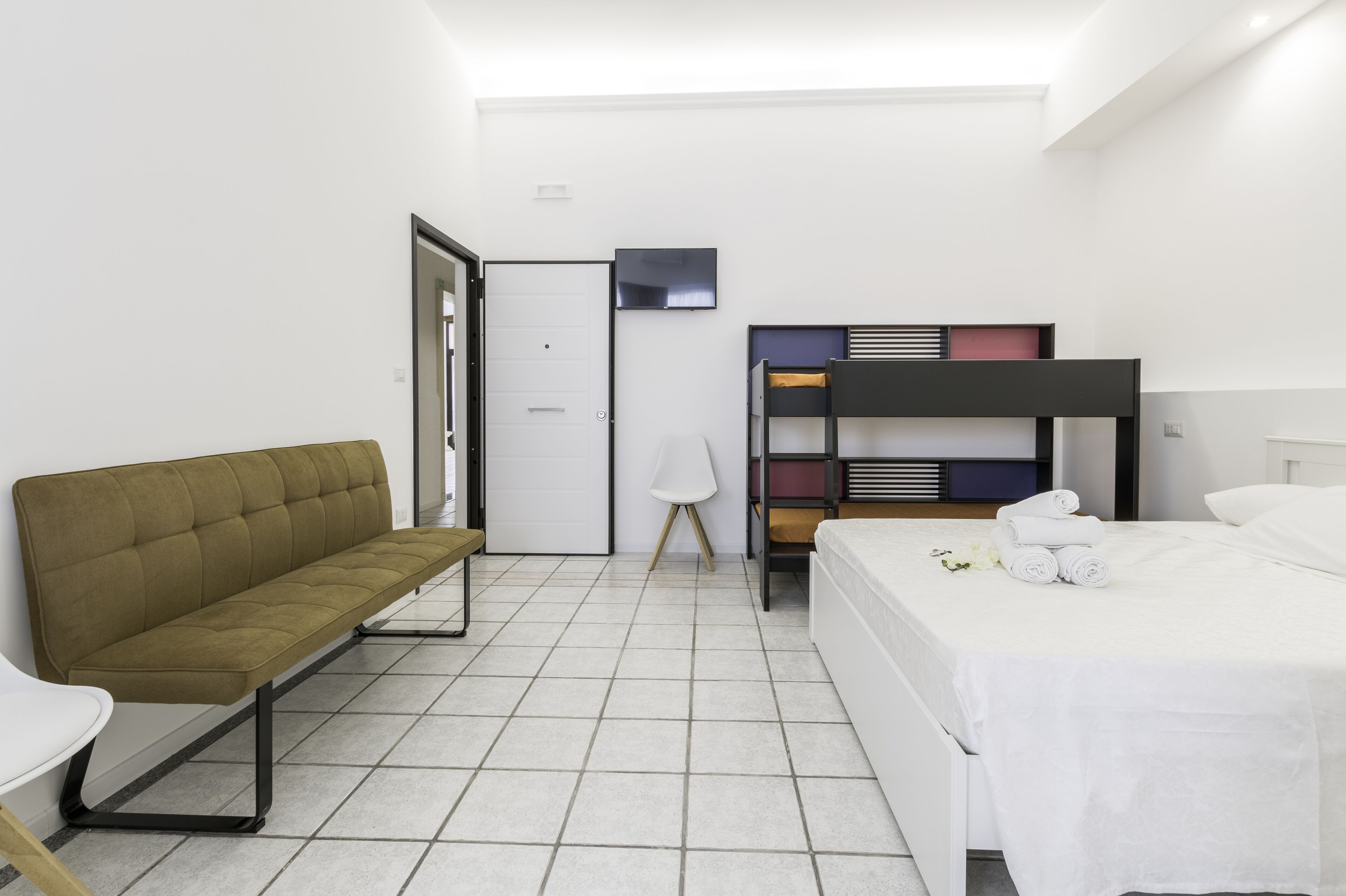Habitació d'hotel moderna amb un llit superposat, un sofà, una taula i una cadira.