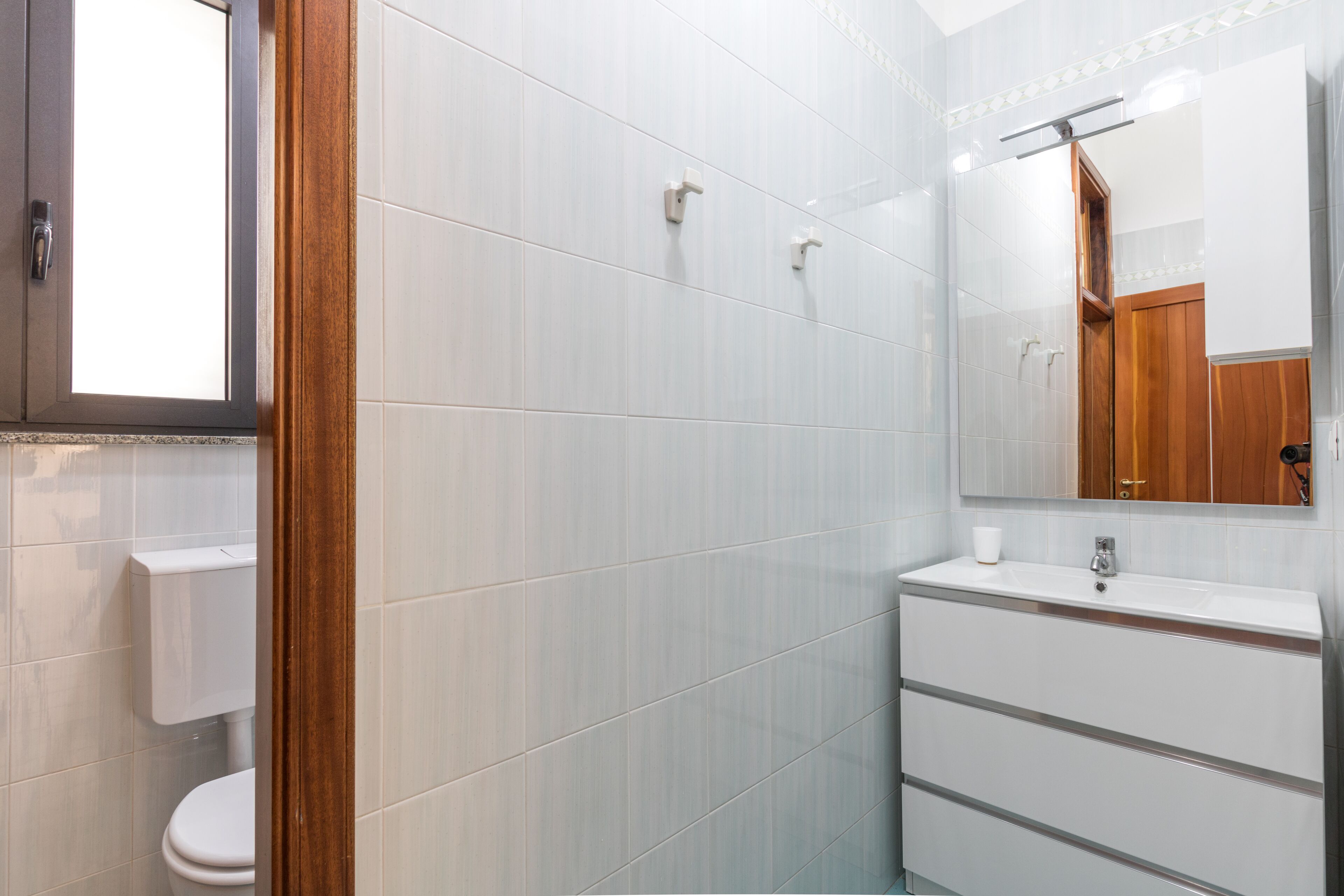 Ein Badezimmer mit weißen Fliesen, einem Holzlaufschild, einer Toilette und einem Spiegel.