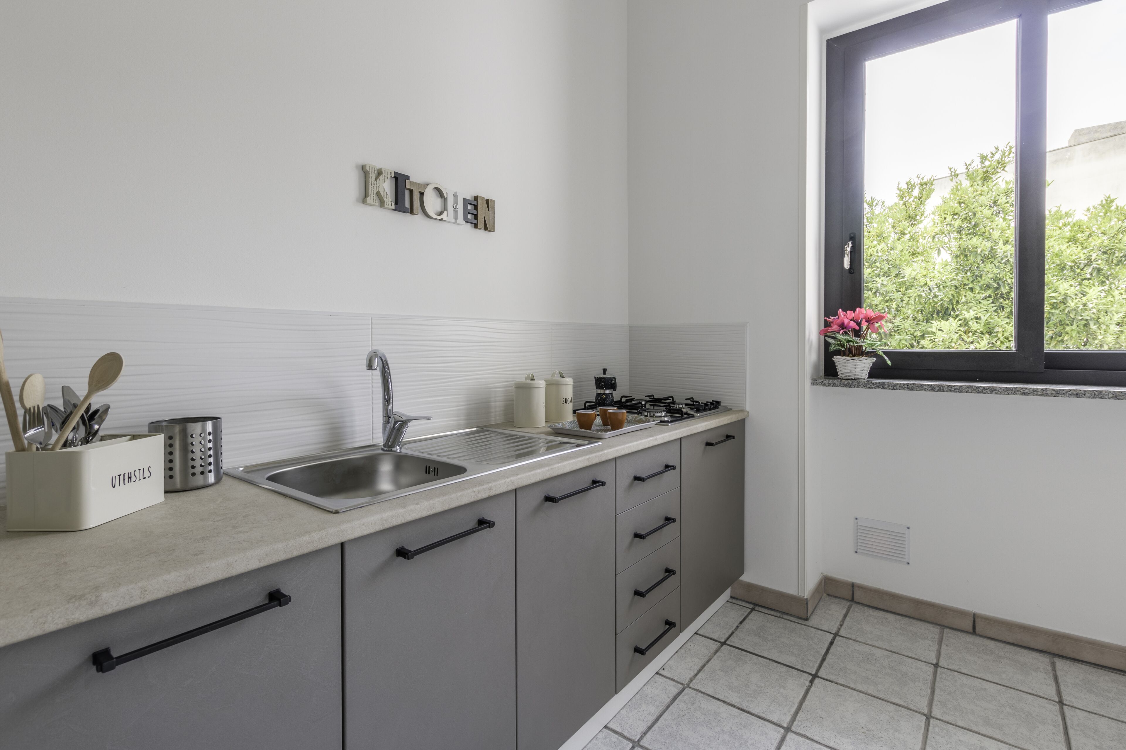 Una cocina moderna con armarios grises, un lavamanos de acero inoxidable y una ventana con vistas a zonas verdes.