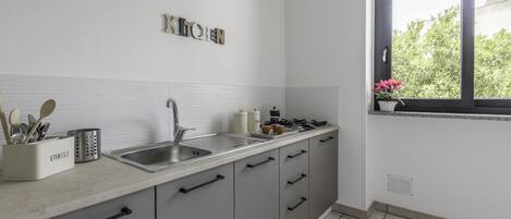 A modern kitchen with grey cabinets, a stainless steel sink, and a window with a view of greenery.