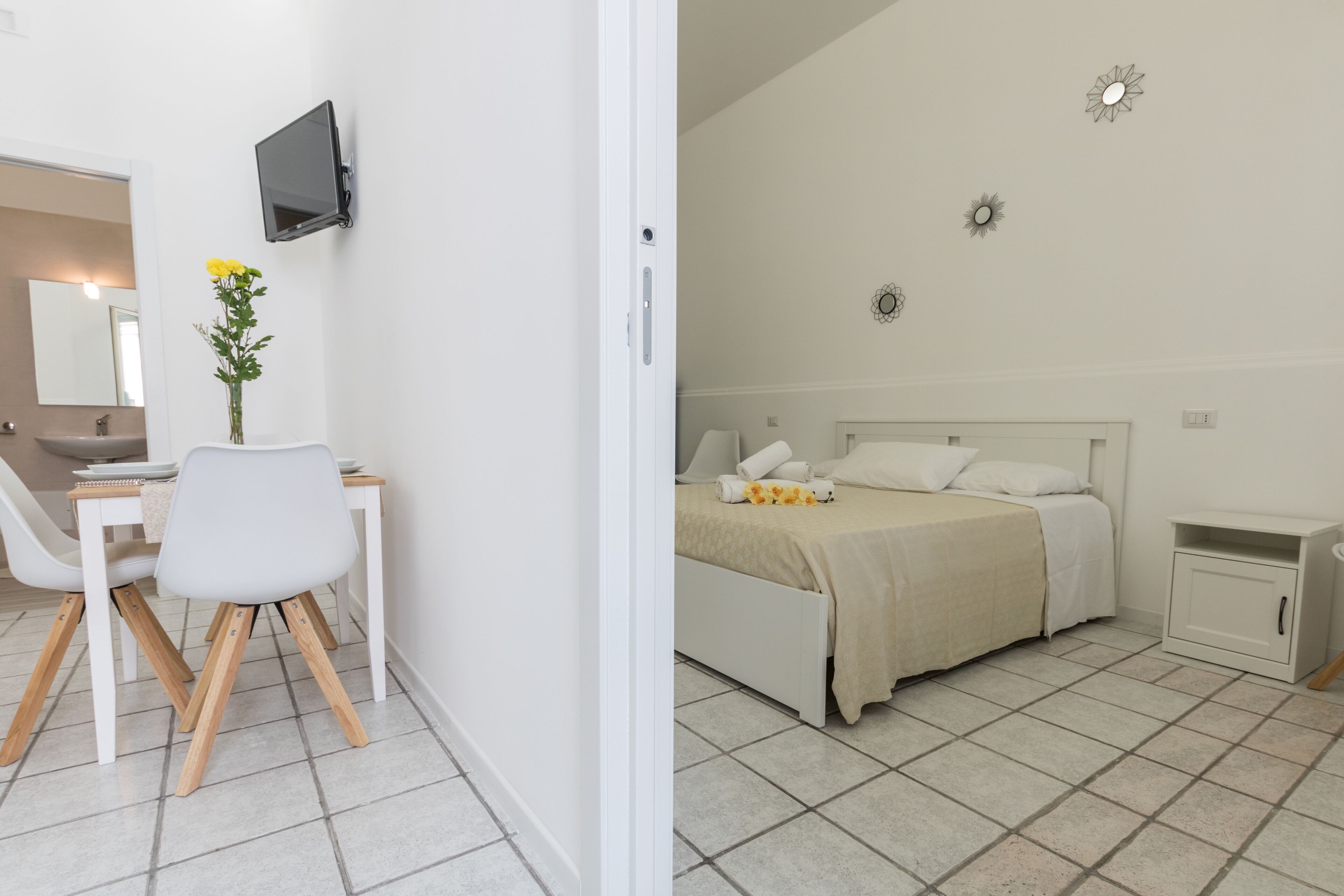 Een kamer met een bed, nachtkastje en een klein kastje. Er is een bureau met een stoel en een plant.
