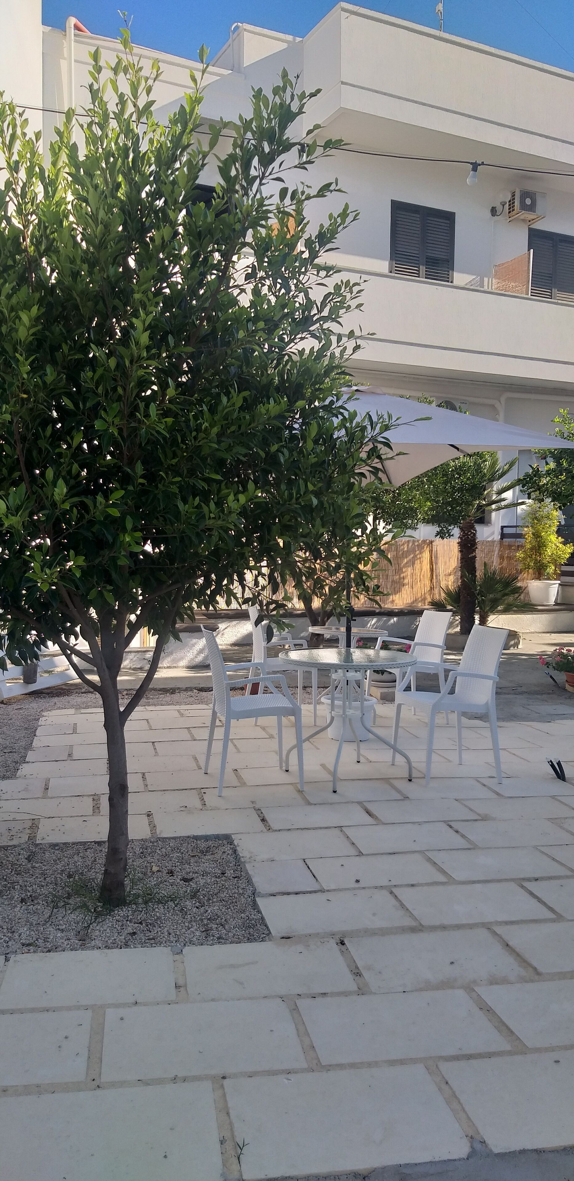 A patio area with a small tree, white outdoor furniture, and a building in the background.