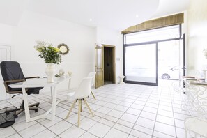 A bright room with a white tiled floor, a white desk with a vase of flowers, a black office chair, and a white chair. - La Gemma del Salento (Racale)